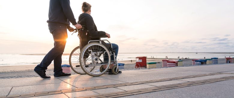 Eine Person im Rollstuhl wird über die Promenade geschoben